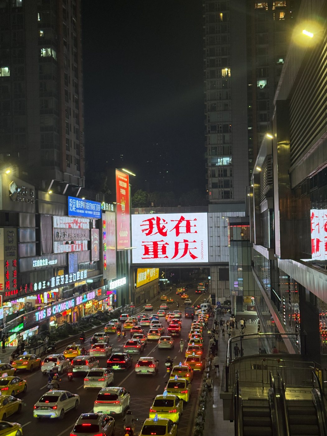 A Chongqing street at night: a traffic jam between skyscrapers and a neon sign reading 我在重庆, “I'm in Chongqing”