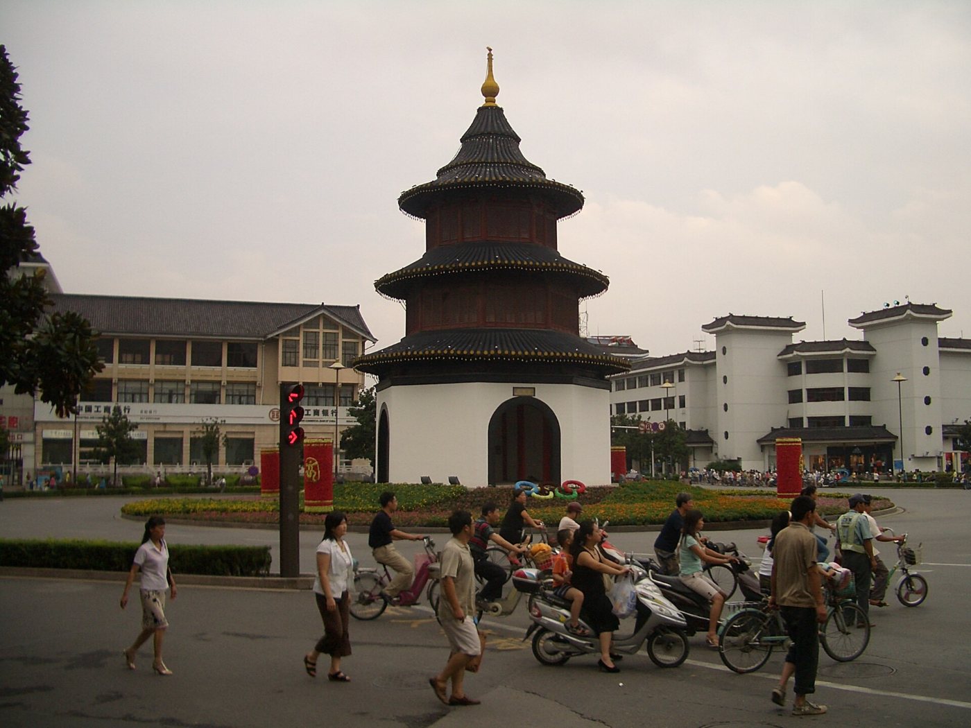 A junction in Yangzhou: cyclists and electric scooters riding past pedestrians, with the Wenchang pavilion behind
