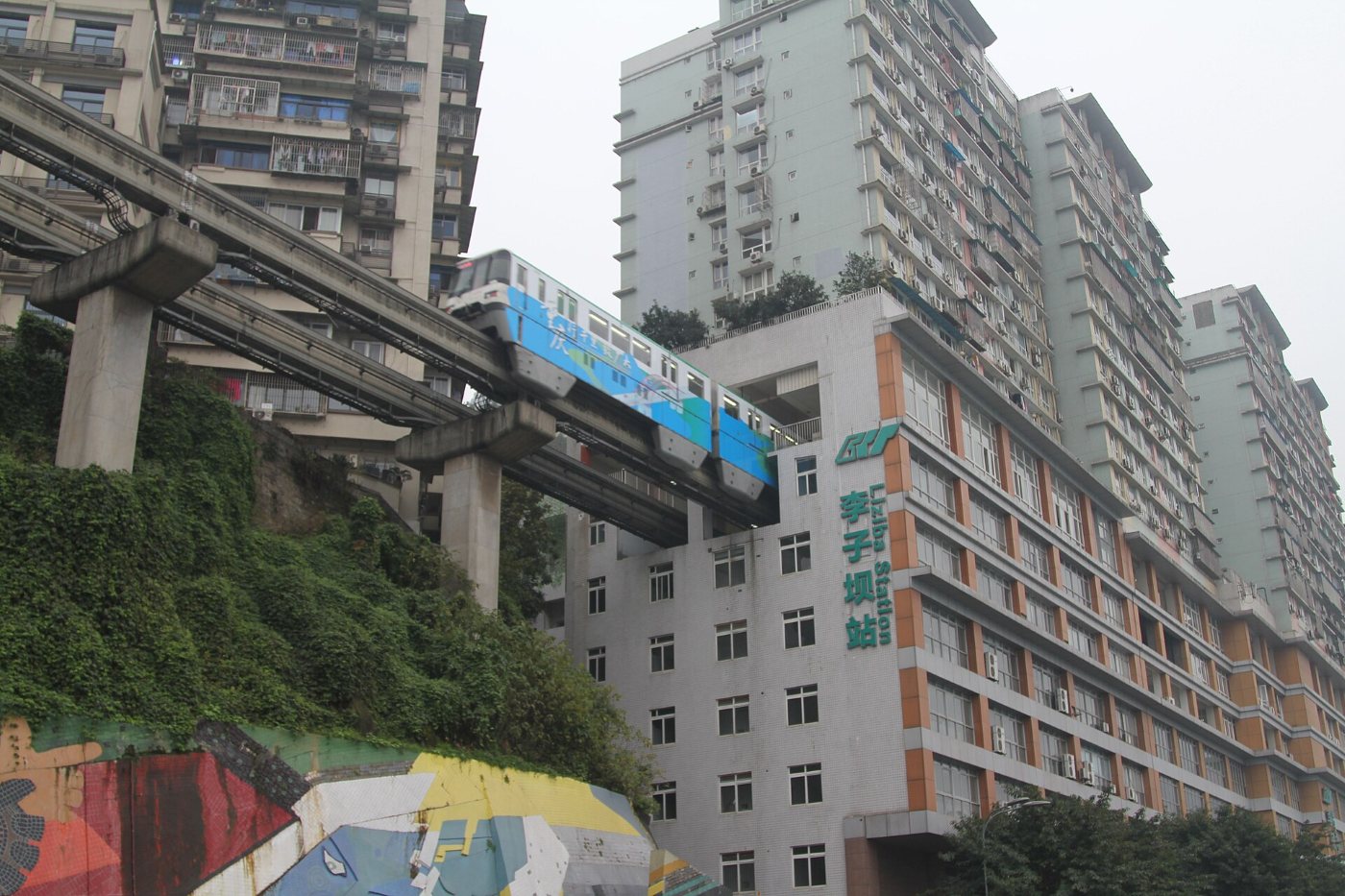 A monorail train entering a residential block at Liziba station, with tower blocks and a green slope beside it