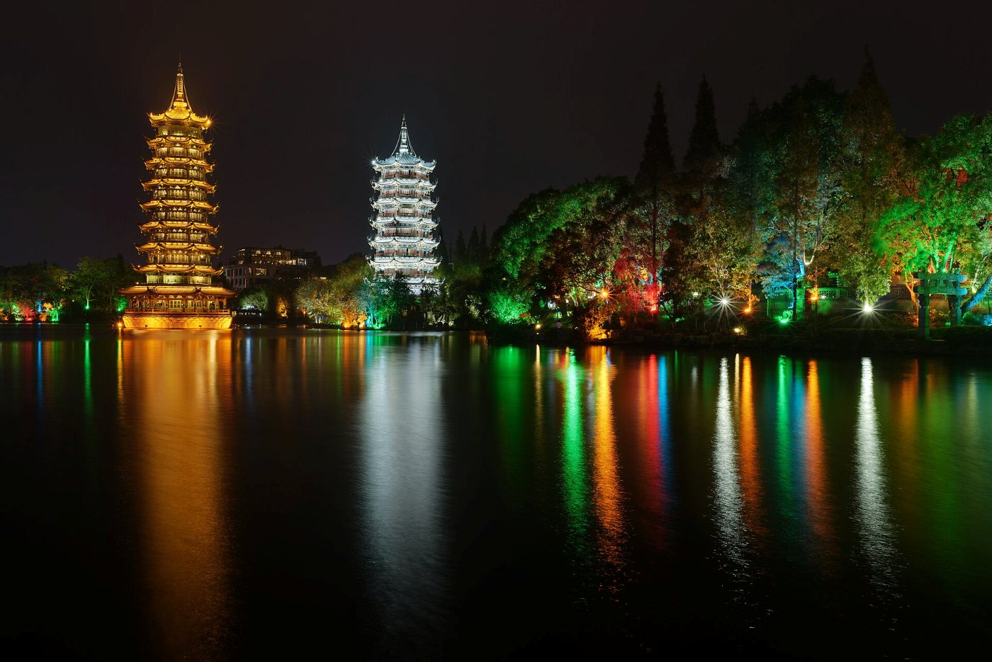 The Sun and Moon Pagodas in Guilin at night: a golden and a white pagoda lit up above a lake, reflected in the water