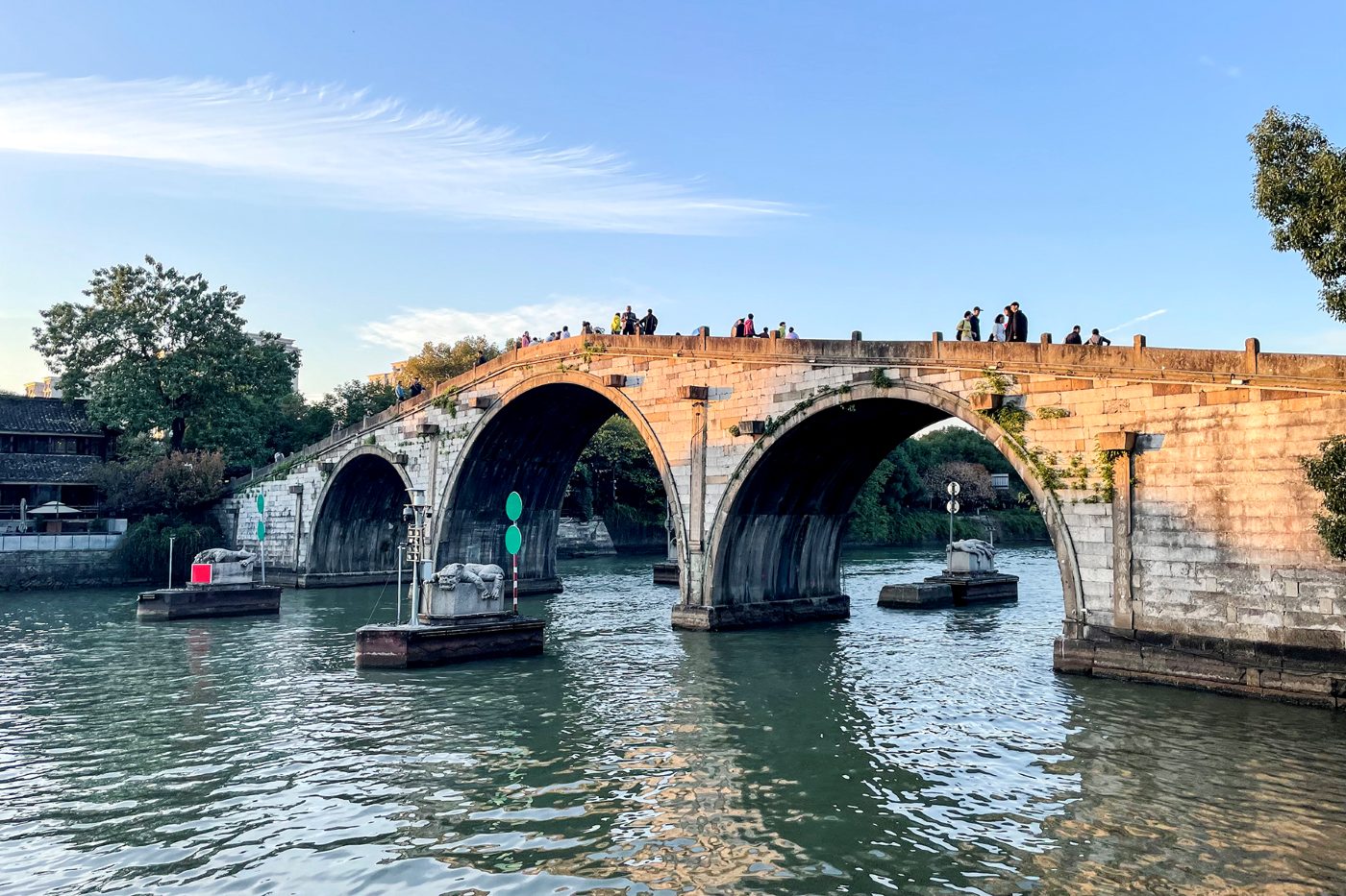 The three-arched stone Gongchen Bridge over the Grand Canal in Hangzhou, with boats on the water and people walking on the bridge
