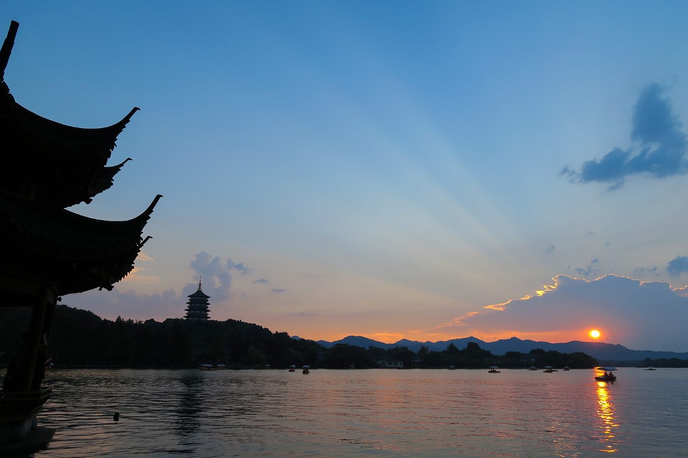 Sunset over West Lake in Hangzhou: the silhouette of Leifeng Pagoda on a hill, sunbeams over the mountains and reflections on the water