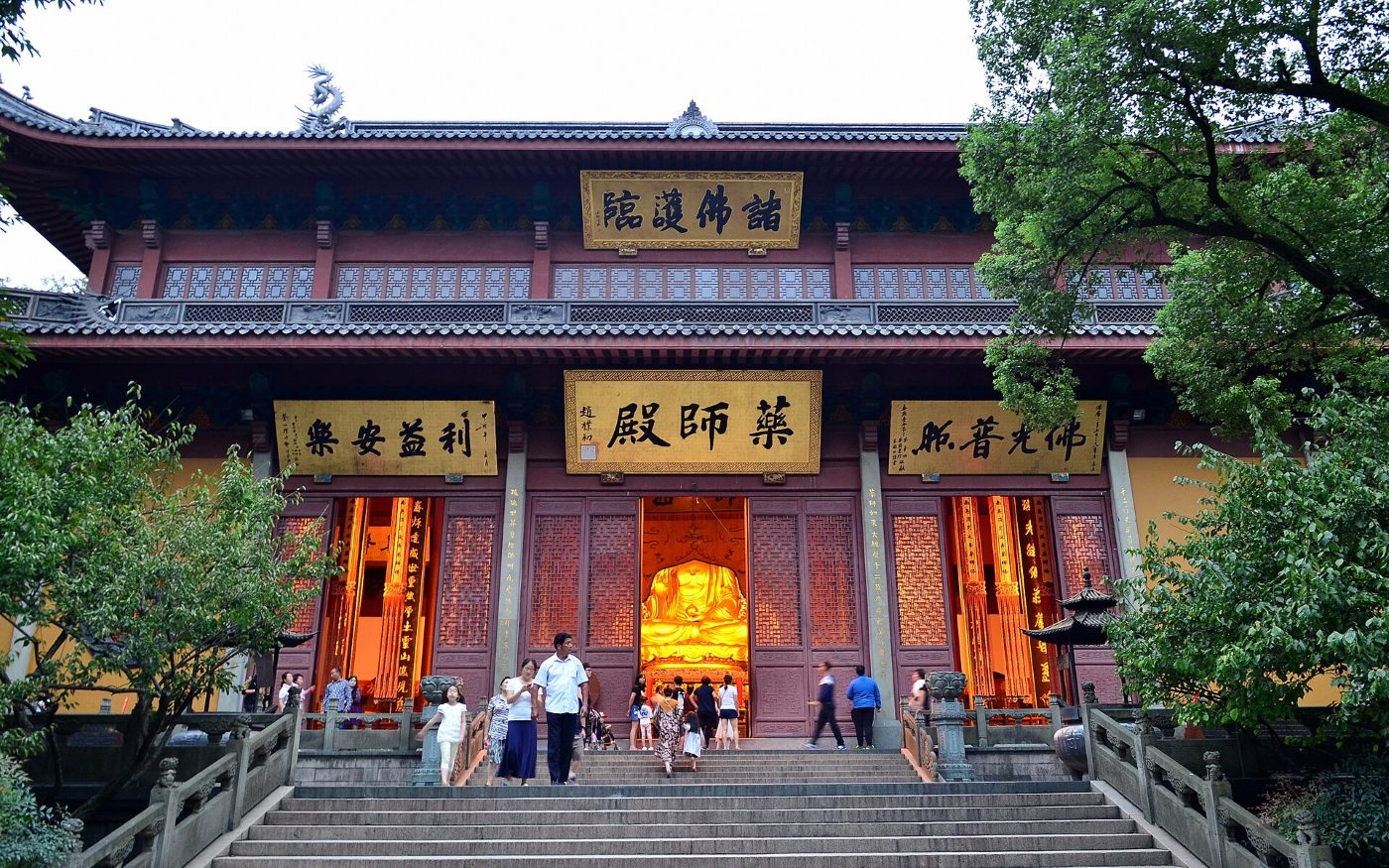 The Medicine Buddha Hall at Lingyin Temple: red columns, gold inscribed boards and a lit statue inside, with steps and visitors in front