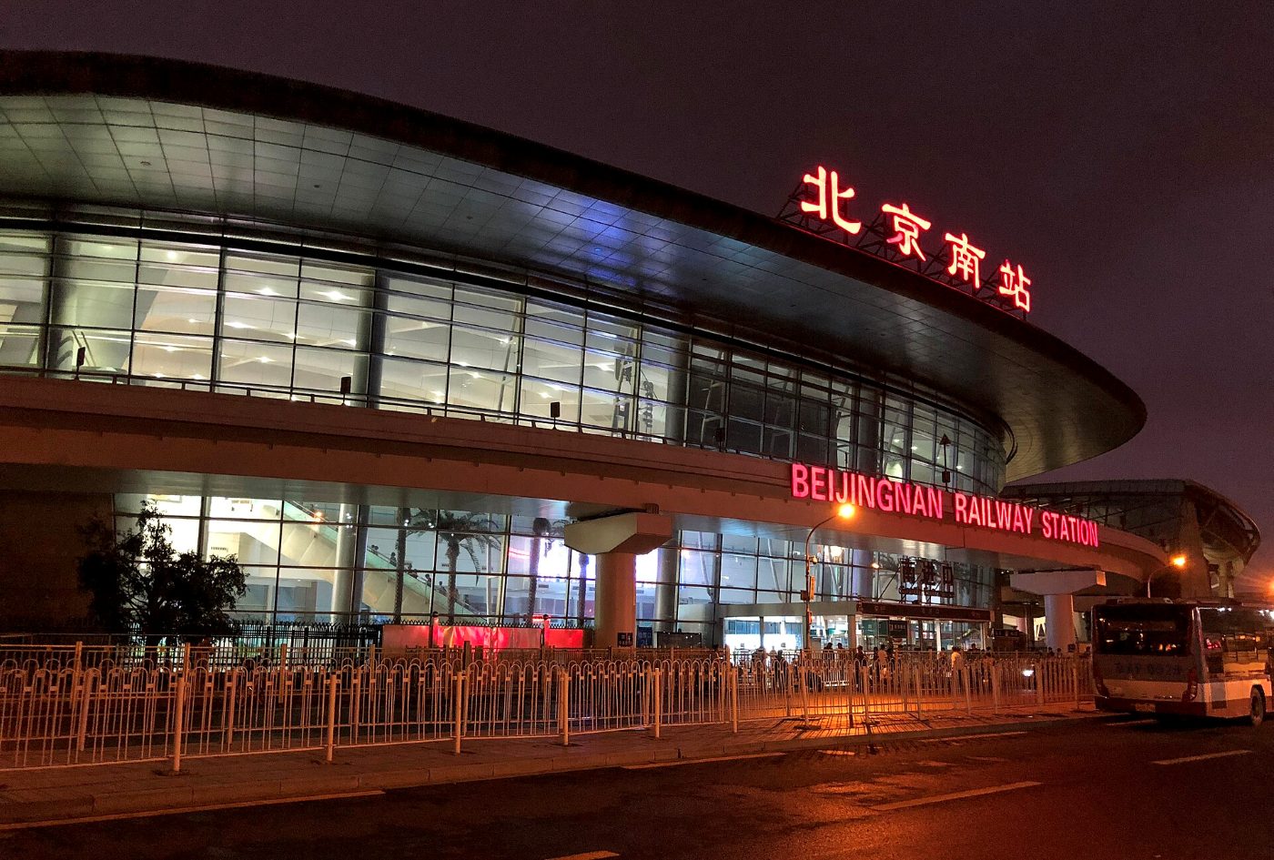 The south facade of Beijing South station at dusk: a long glass front under a curved roof, with the station name in red characters