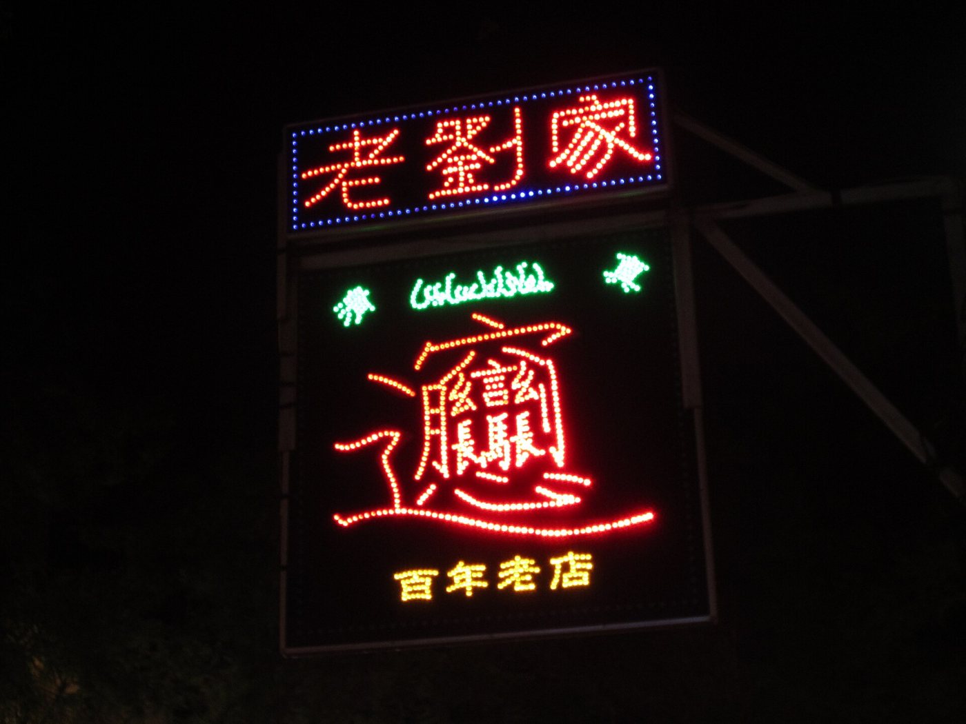 A red neon sign at night with the very complex character “biang” above a noodle bar