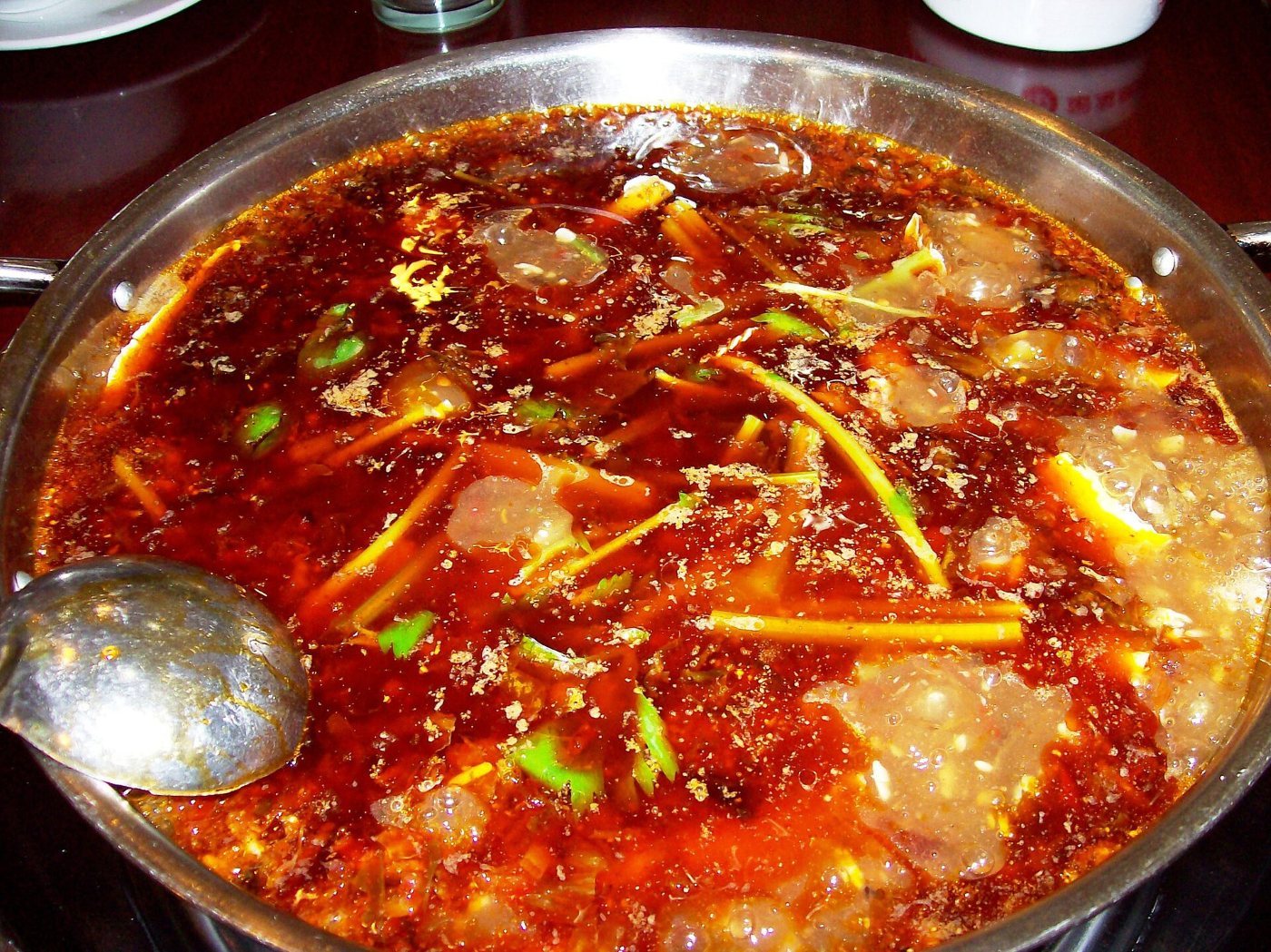 A hotpot: red, oily broth full of chillies, with a ladle beside it