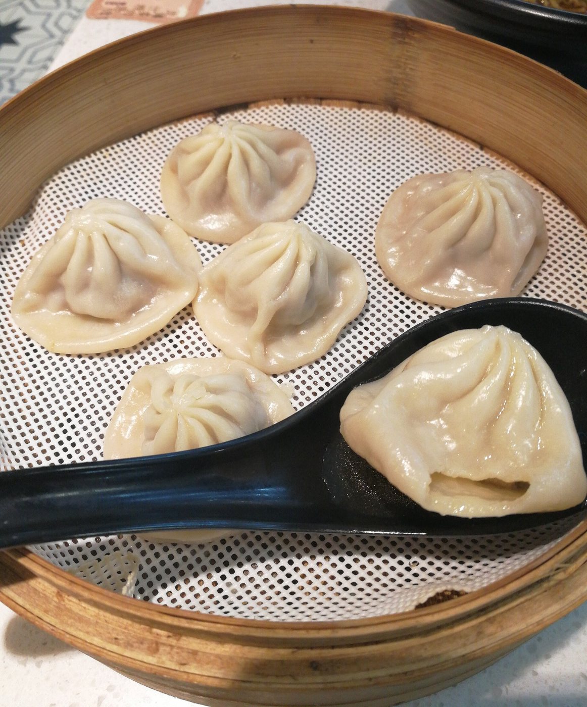 Xiaolongbao dumplings in a bamboo steamer, one on a black spoon