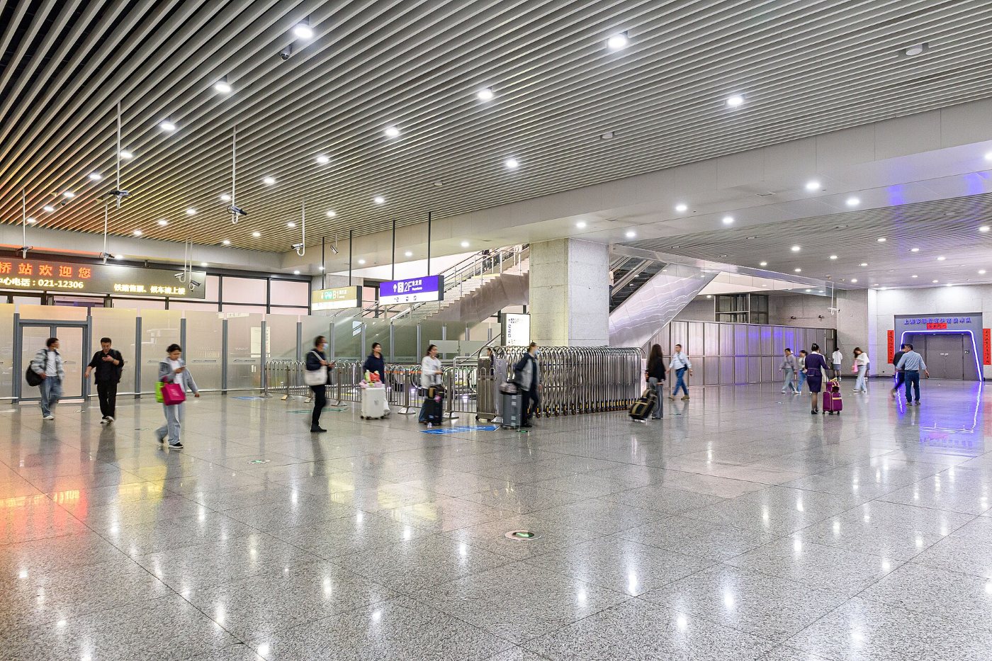 The hall of Shanghai Hongqiao railway station: travellers with suitcases and backpacks crossing a shiny floor, with escalators to one side