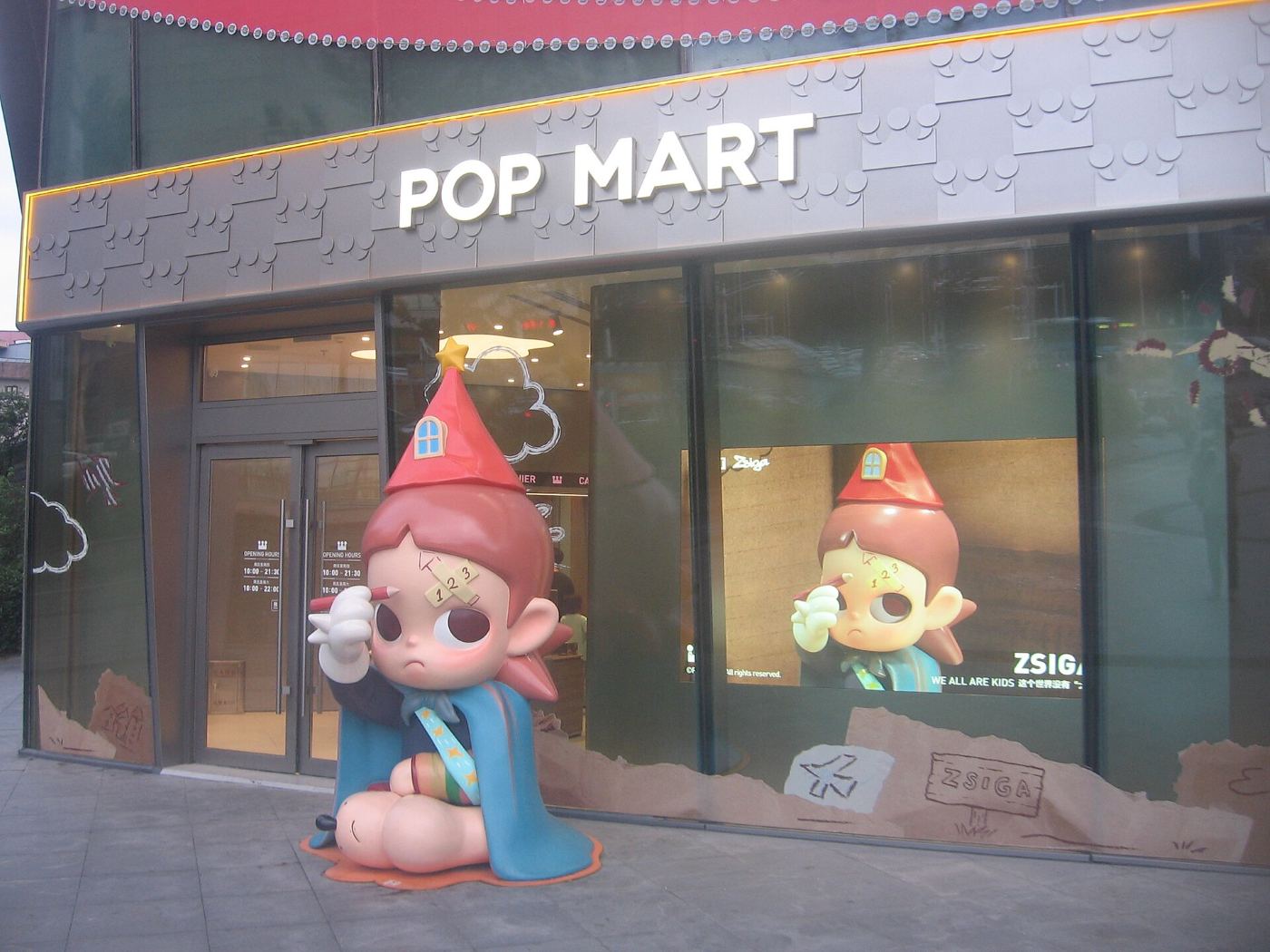 A Pop Mart shop in a Chinese mall with a large figure of a character in a red hat by the entrance