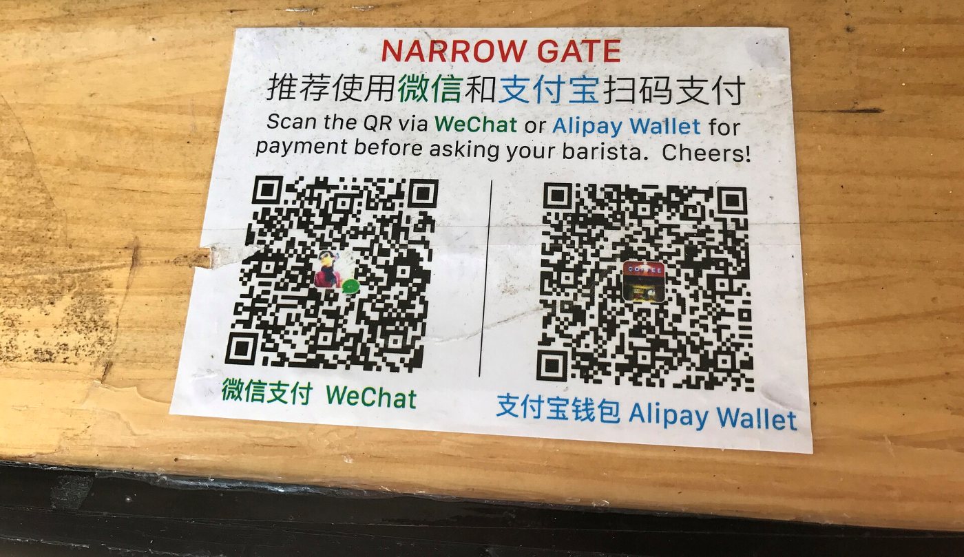 A card on a wooden counter with two payment QR codes: WeChat Pay and Alipay