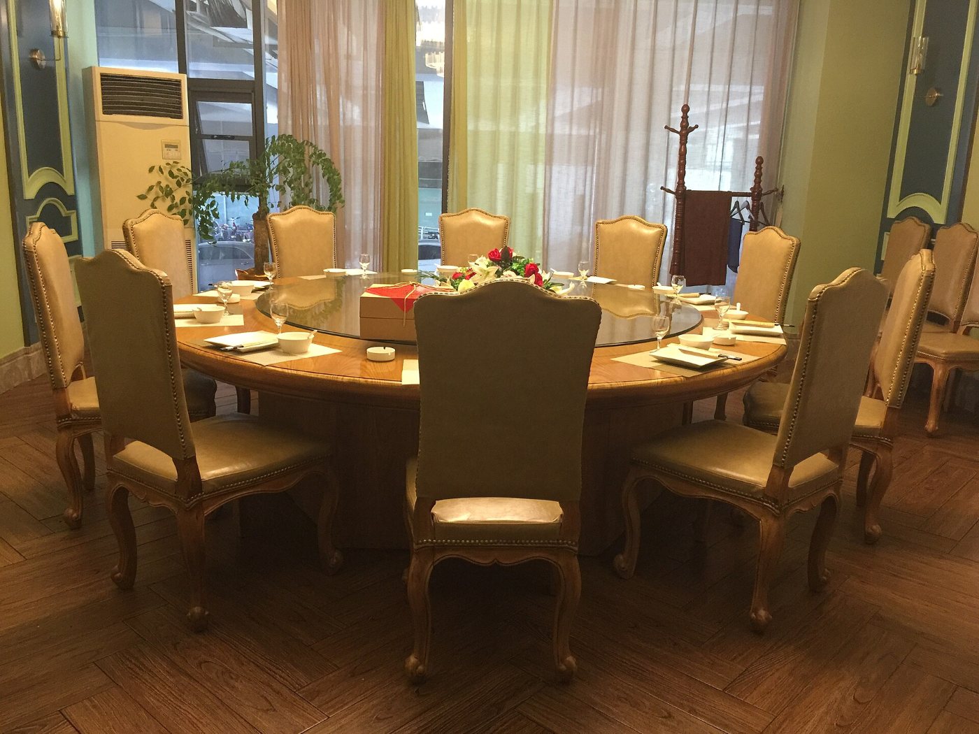 A round table in a restaurant room with a glass lazy Susan in the middle, surrounded by chairs and place settings