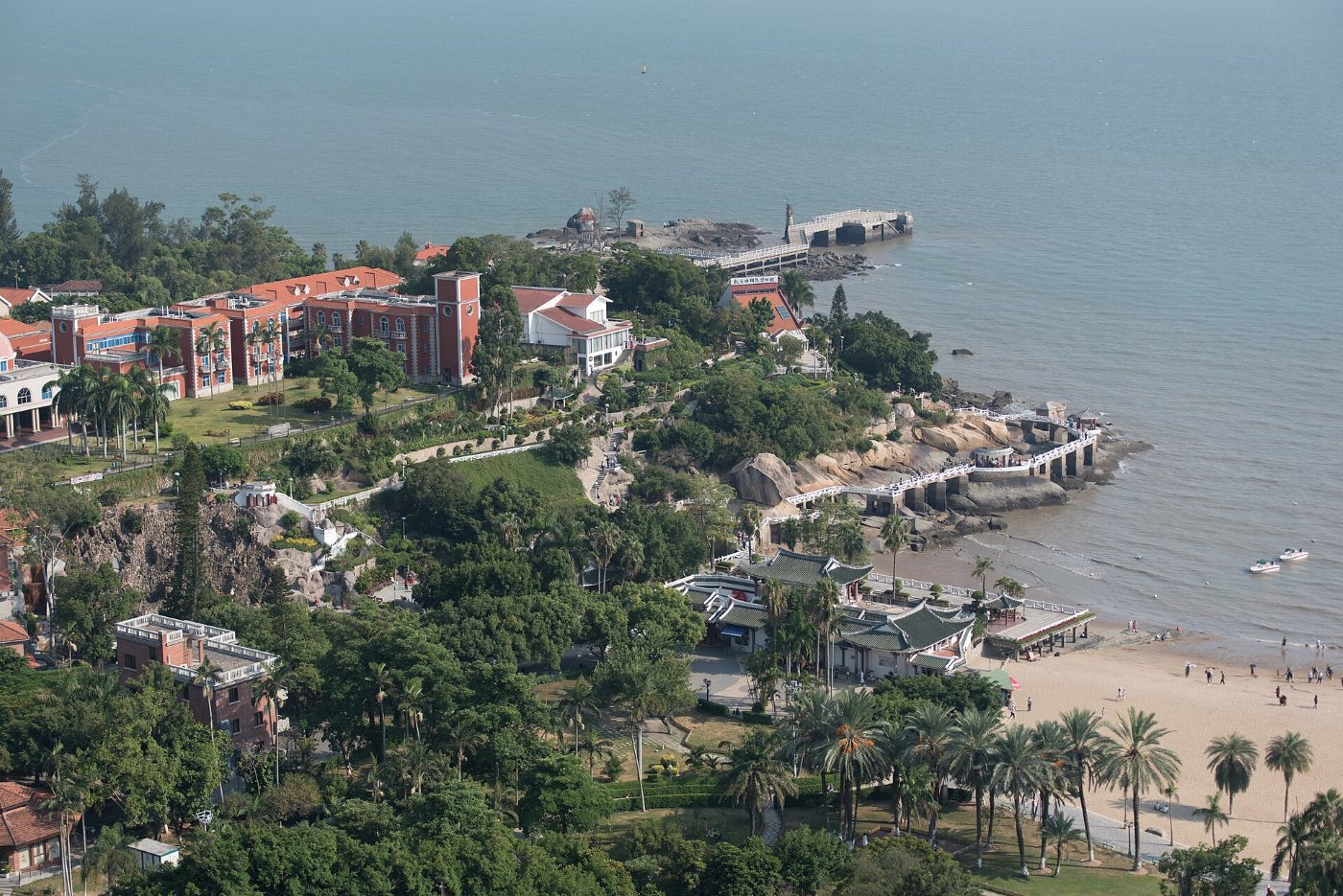 Ogród Shuzhuang na Gulangyu z góry: pawilony z czerwonymi dachami, zygzakowaty mostek nad morzem, mała plaża i palmy