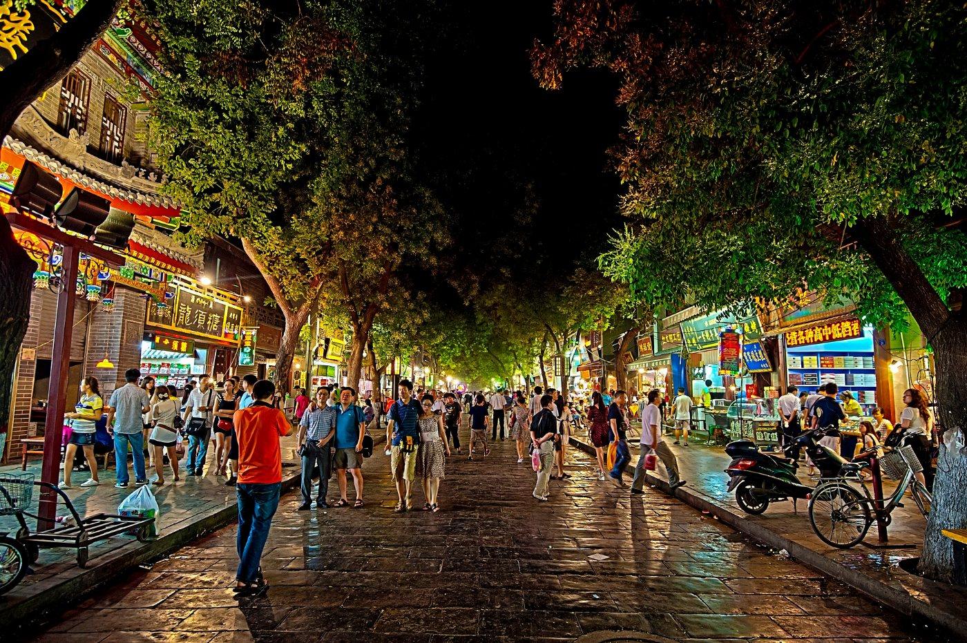 A street in Xi'an's Muslim Quarter at night: crowds under trees, lit shops and food stalls on both sides