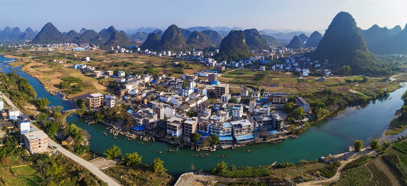 Aerial panorama of Yangshuo: a river winding around the town, dozens of green conical karst hills behind it