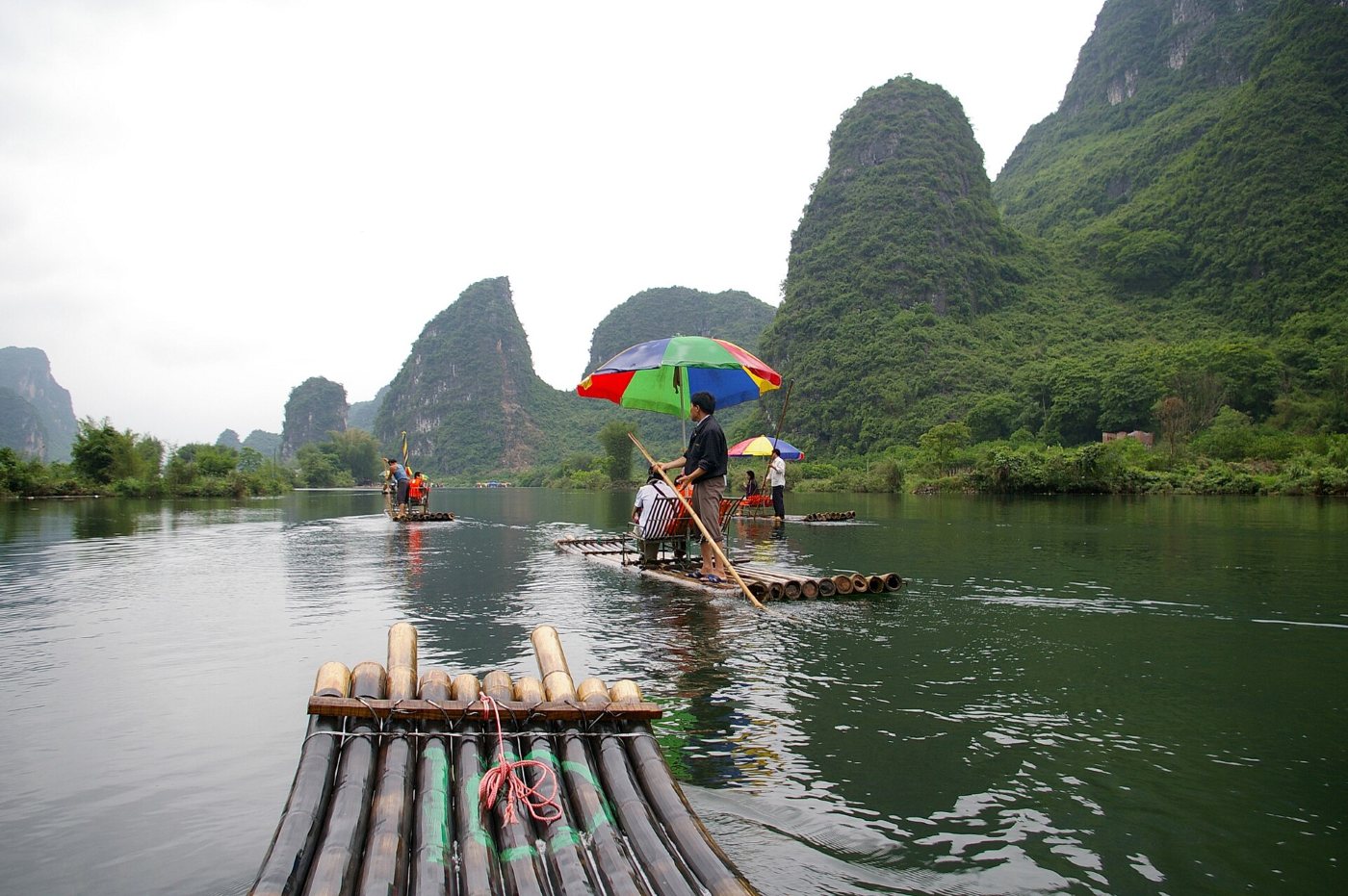 A bamboo raft with a colourful umbrella on the Yulong River near Yangshuo, karst hills behind