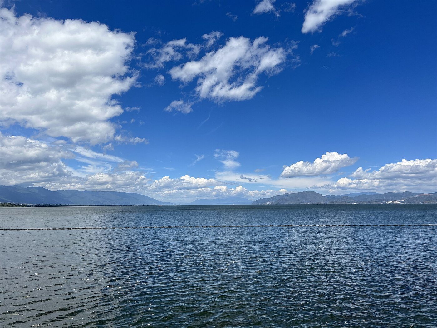 The wide expanse of Erhai Lake under a blue sky with white clouds, mountains in the distance