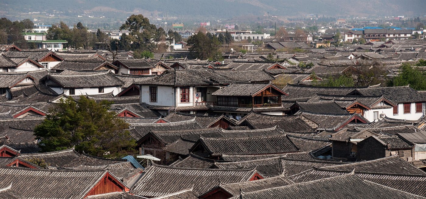 A sea of grey roofs of the wooden houses of Lijiang Old Town, with green hills behind