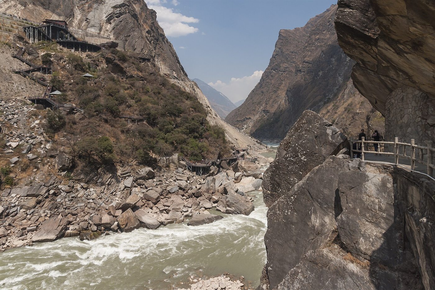 A raging river in a deep rocky gorge, with a wooden walkway clinging to the cliff above the water