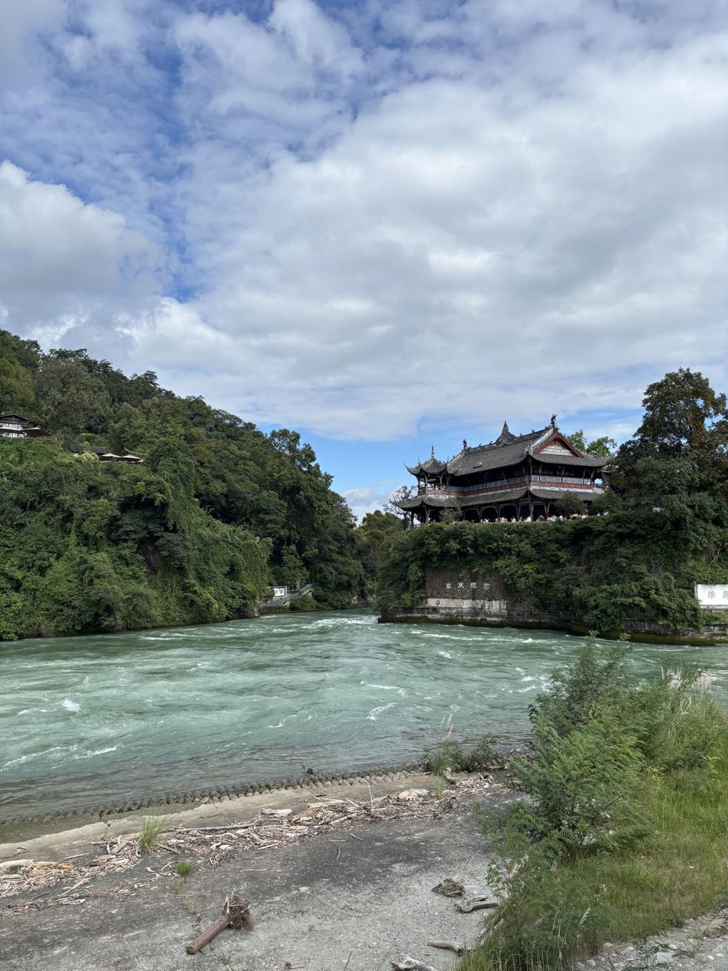 The Min River at Dujiangyan: a fast, greenish current between wooded banks, a pavilion on a hill behind