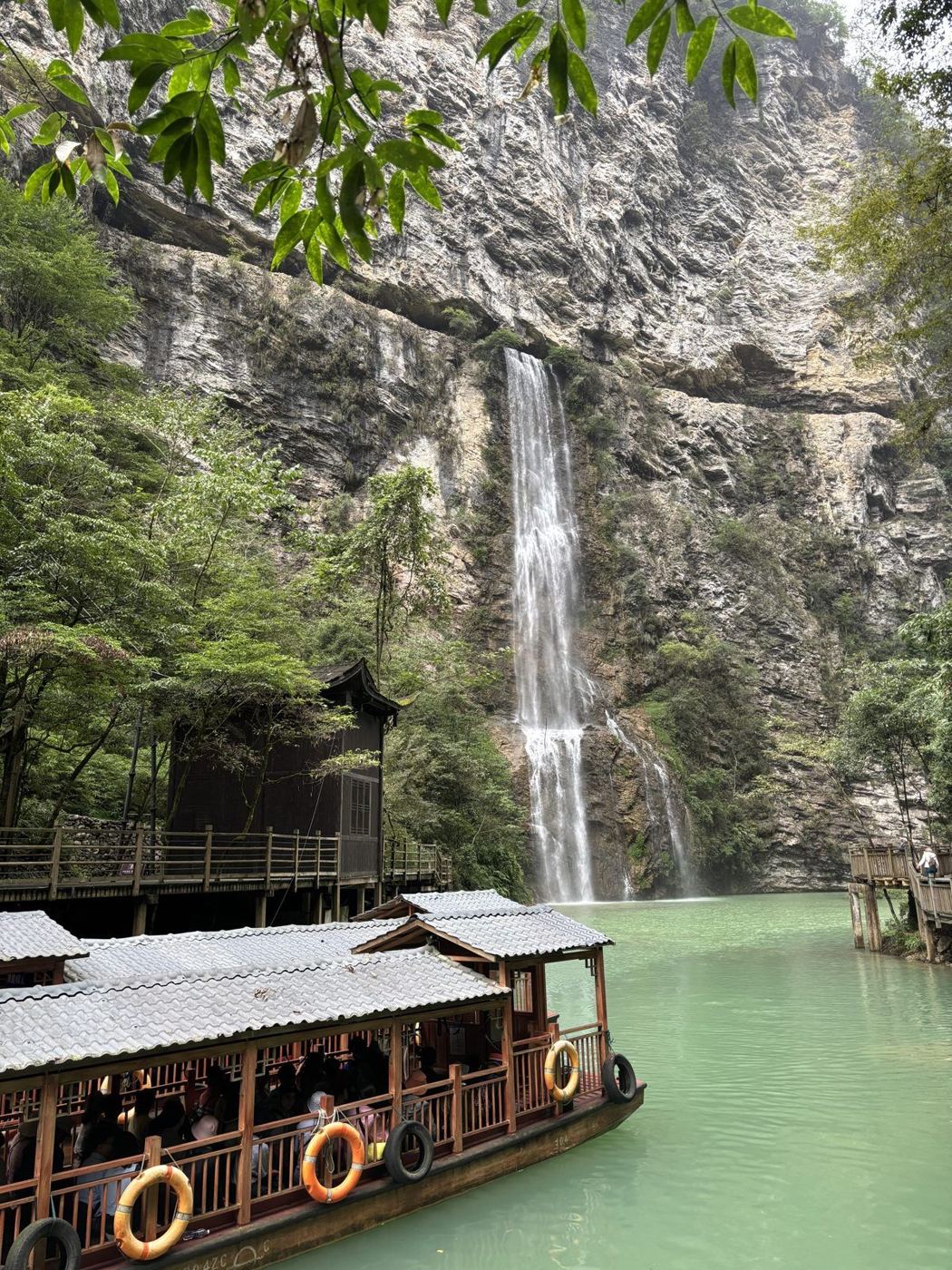 A waterfall pouring down a rock face into a green lake on the floor of the Zhangjiajie Grand Canyon, a wooden boat in the foreground
