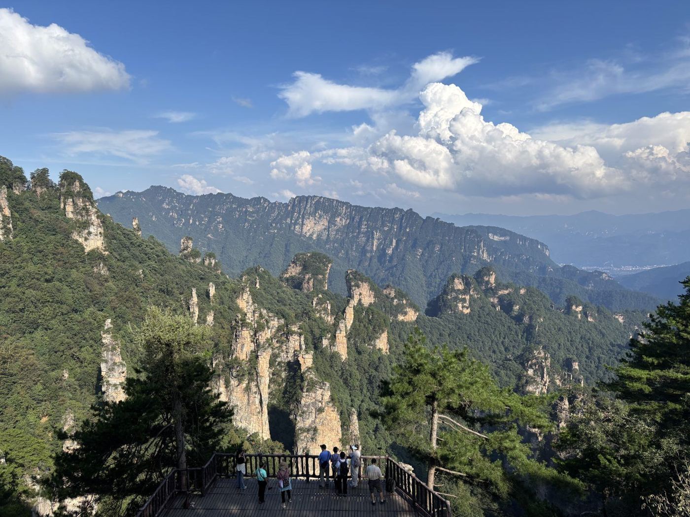 Stone pillars in Zhangjiajie National Forest Park under a blue sky with white clouds, a viewing terrace with tourists on the left