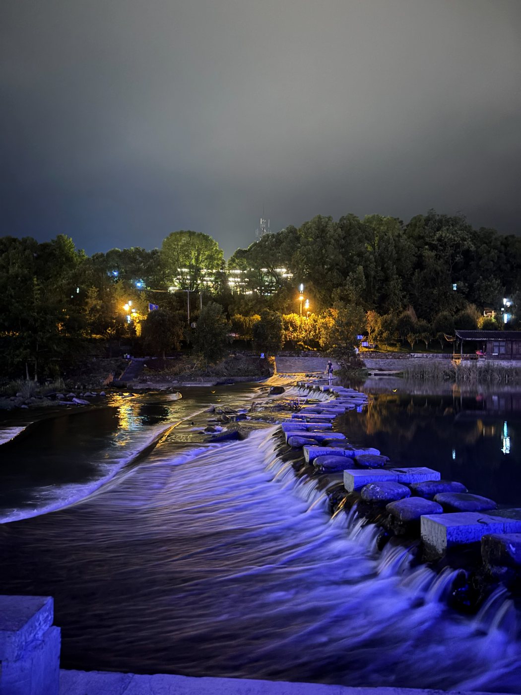 The river in Wulingyuan at night: water spilling over a stone weir, with lights on the bank